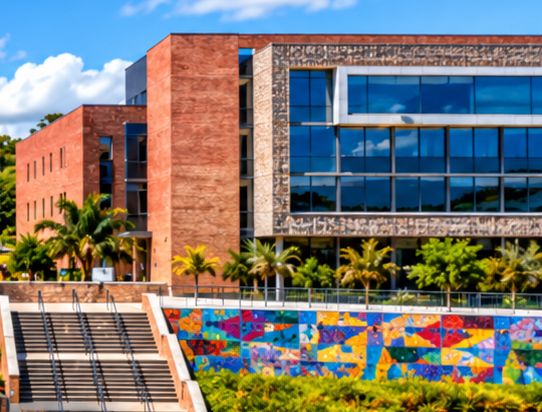 Red-brick and glass buildings on the University of Mpumalanga campus, with a colourful mosaic wall and palm trees.